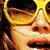 A person wearing yellow sunglasses with a heart-shaped cutout, holding white flowers near their face.