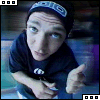 A person wearing a dark beanie with white text and a dark shirt points forward while looking up, captured in three showing slight head movement