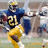 Pixelated image of a football player in blue and yellow uniform running with ball, background shows blurred stadium scene.
