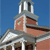 Pixelated image of a building with a tower, red brick facade, white trim, and a blue sky background.