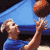 Pixelated static image of a person in blue clothing holding an orange basketball above their head against a blue background with dark horizontal bands.