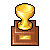 Pixelated golden trophy with rounded top on brown rectangular base featuring horizontal panel and small rectangular plaque.
