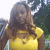 A pixelated image of a person with long dark hair wearing a yellow sleeveless top, standing against a blurred background.
