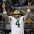Pixelated image of a person wearing a white jersey with green number 4, yellow helmet, and raised arms against dark background.