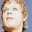 Pixelated close-up of a person's face with light brown hair, neutral expression, and visible eyes nose mouth against blue background.