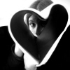 Black-and-white static image of a person with light hair holding a large heart-shaped object, partially obscuring their face.