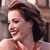A pixelated close-up of a person with dark hair tied back, wearing a red top, smiling with eyes closed against a blurred background.