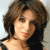 Static pixelated image of a person with shoulder-length brown hair, light skin, and a black top against a light gray background.