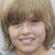 Static pixelated image of a person with light brown hair, smiling face showing teeth, and visible ear with dark earring.