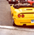 Yellow vehicle with red taillights and dark brown accents, viewed from a low angle against a muted background.