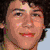 A young man with curly brown hair appears in multiple poses: smiling, neutral expression, and looking away. He wears a pink tank top, striped shirt, and dark clothing across different frames.