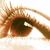 A pixelated close-up of a human eye with brown and green hues, showing detailed iris patterns and a white reflection in the pupil against a light background.