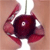 A static image of a dark red, glossy, circular object with a central white dot, held by two red, curved appendages against a light brown background.