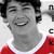 A person in a red and white shirt smiles broadly, with visible teeth, against a light background with partial text elements.