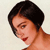 Pixelated close-up of a person with short dark hair, light skin, and red lips, angled slightly downward against a light background.
