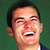 Pixelated close-up of a person's face with dark hair against a green background, mouth open in laughter showing teeth and tongue.