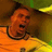 Pixelated static image of a person in an orange shirt with dark hair and a black necklace, set against a brown background with green and yellow elements.