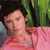 Pixelated image of a person with dark hair wearing a pink garment against a green and dark background.