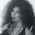 A grayscale pixelated image of a person with voluminous dark hair holding a microphone, wearing a dark top with light accents.