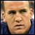 Static pixelated image of a person with light skin tone wearing dark blue clothing, cropped to show head and shoulders against blurred background.