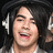 A person with long dark hair wearing white headphones and a light-colored jacket, smiling with mouth open in a of four