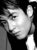 Black-and-white pixelated image of a person's face in profile view, wearing dark clothing against a dark background.