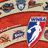 A pixelated image with an orange background, featuring a central shield-shaped logo with red, white, and blue colors, surrounded by smaller icons and text elements.