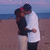 Two people embrace on a beach at dusk, with the ocean and sky in the background.