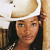 A person wearing a light-colored cowboy hat with a dark band, long dark hair, and a dark top with a patterned design.