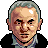 Pixelated portrait of an older man with gray hair, light skin, and dark eyebrows wearing a black jacket over a blue shirt against a solid gray background.