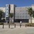 Pixelated static image of a modern building with multiple windows, surrounded by trees and a paved area under a clear blue sky.