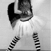 Black-and-white image of a person in a tutu and striped socks holding a patterned bag, viewed from the waist down.