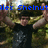 A pixelated image of a person in a black shirt and dark pants with arms raised, overlaid with blue text reading "Alex ShelnutIs AMAZING" against a blurred outdoor background.