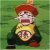 Pixelated figure with red hair, yellow top, dark sleeves, and a circular emblem on chest against green background.