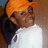 Pixelated image of a person with orange hair wearing a white shirt and dark jacket, set against a brown background.
