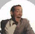 Pixelated static image of a person with dark hair wearing a light-colored shirt under a dark jacket, set against a white background with gray border.
