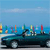 A pixelated image of a dark green convertible car with a light blue sky background and colorful vertical bars on the horizon.