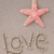 A static beach scene with a pink starfish, 'love' written in sand, two interlocked hearts drawn in sand, and a tropical background.