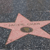 A pink star-shaped icon with a dark oval center on a pixelated gray background.