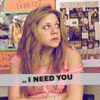 A woman with long brown hair in a pink top appears against a blurred background of shelves and signs, with text overlay reading "I NEED YOU".