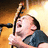 Pixelated image of a person with dark hair holding a microphone, wearing a blue shirt against warm-toned background.
