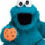 Static pixelated image of a blue cartoon character holding an orange cookie with chocolate chips, featuring large eyes and a dark mouth opening against white background.