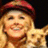 Pixelated image of a smiling person with blonde hair wearing a red cap, holding a small dog, with text overlays on pink and gray backgrounds.