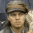 Pixelated portrait of a person wearing a light brown cap with dark brim, long dark hair, and a light-colored shirt against a blurred background.