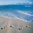 Pixelated beach scene with light brown sand, blue water, and white wave crests under a pale sky.