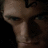 Pixelated close-up of a person's face with dark hair and a light-colored neck, set against a dark background.