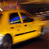 Yellow taxi cab in motion with blurred background, blue light visible through side window, dark tire and wheel well, yellow roof sign partially visible.