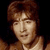 Pixelated close-up of a person with light brown hair styled in a voluminous, rounded shape against a dark background.