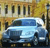 Pixelated image of a light blue sedan parked in front of a building with yellow and brown tones, featuring dark windows and a streetlamp.