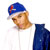 Pixelated figure wearing blue cap with red and green details, white shirt, and dark blue jacket, head turned right with neutral expression.